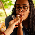 A close-up lifestyle shot of a person having their cigarette lit with a gold lighter. The lighter has a polished gold body, a clear plastic cap, and a visible flame.