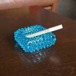 Blue textured ashtray with a cigarette on a wooden surface