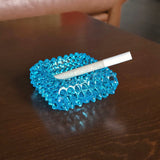 Blue textured ashtray with a cigarette on a wooden surface