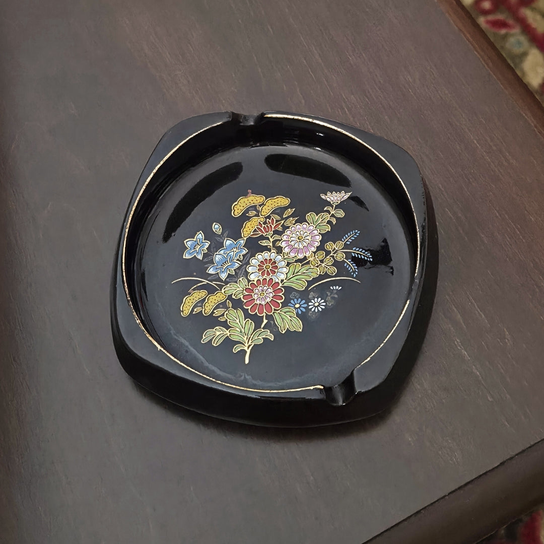 Black ceramic ashtray with floral design on a wooden surface