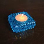 Blue textured candle holder with a lit candle on a dark surface