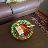 Colorful decorative plate with herbal cigarettes on a wooden table, with a brown sofa and patterned rug in the background.