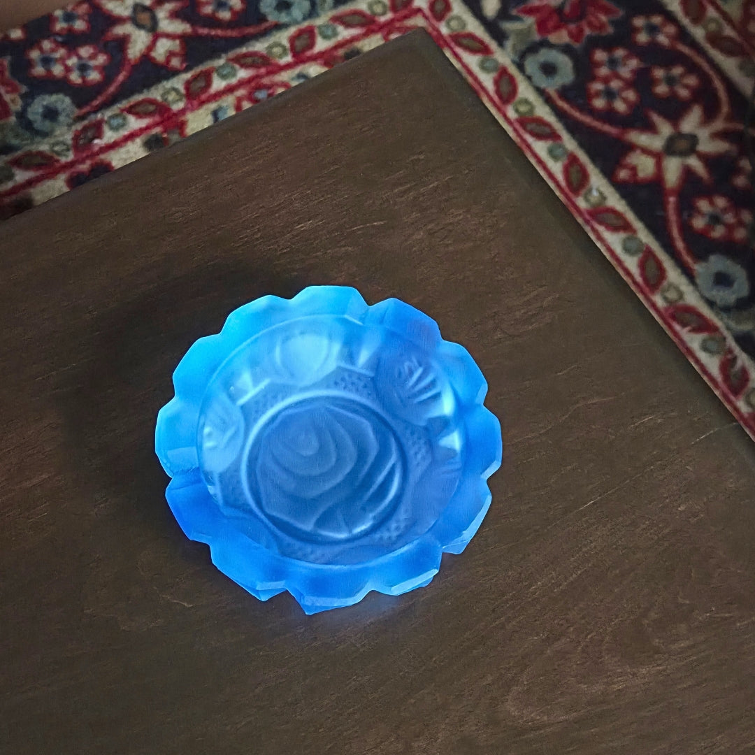 Blue decorative ashtray on a wooden surface with a patterned rug in the background
