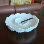 White ceramic bowl with textured rim on a wooden surface, with a brown leather couch in the background.