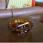 Amber glass ashtray with cigarette on a wooden table with a brown leather couch in the background