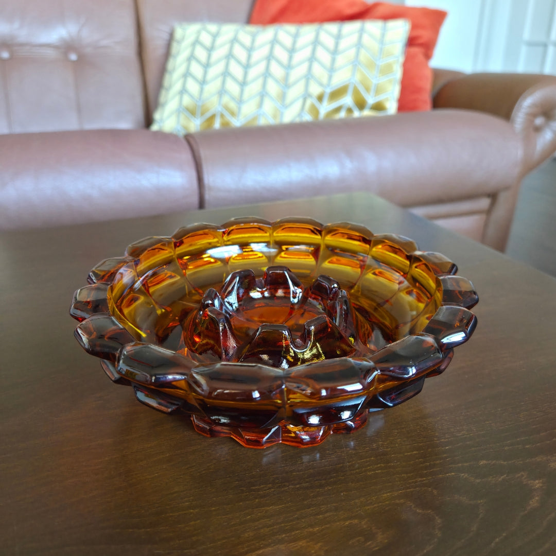 Amber glass ashtray on a wooden table with a couch and pillows in the background